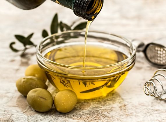 Oliwa z oliwek na keto wlewana do szklanej miseczki obok zielonych oliwek