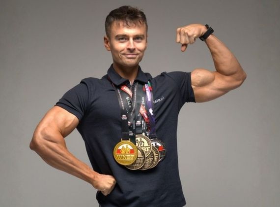 Zawodnik sylwetkowy z medalami po zawodach pozuje z napiętym bicepsem