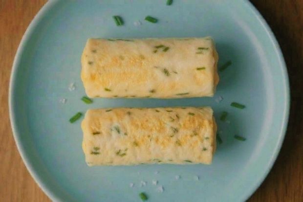 Zawijas serowo-jajeczny keto - dwa rulony z jajek i cheddara posypane szczypiorkiem na niebieskim talerzu